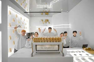 A group of people posing in front of an Arabica coffee machine with various canisters on display, creating a friendly and inviting atmosphere