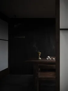 A dimly lit dining room with a dark wooden table, two bowls of food, cups, and a vase, creating a cozy and intimate atmosphere