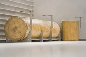A wooden bench with a rustic appearance sits in front of a wall, supported by metal brackets, in a well-lit interior space