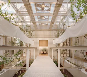 A modern indoor space with a white staircase surrounded by plants and trees, featuring potted plants on the ground and hanging from the ceiling
