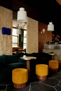 Cozy cafe interior with yellow and green couches, tables, chairs, and lamps, featuring potted plants and vases, with a warm and inviting atmosphere