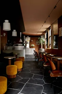 Modern restaurant interior with yellow walls, black flooring, and potted plants, featuring dining tables and chairs