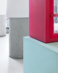 A modern room with two concrete pillars, one with a red door, and two windows, with a car partially visible in the background