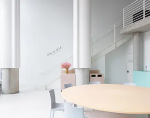 A calm and inviting lobby with a large wooden table and chairs, surrounded by a white room with no visible decorations or furniture beyond the table and chairs