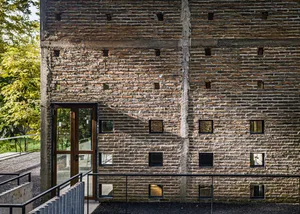 A traditional building with a brick wall and doorway, featuring windows on either side, with natural light and a sense of history
