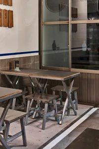 A modern dining area with a metal table and wooden chairs, surrounded by a window allowing natural light to enter
