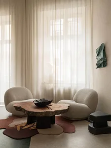 A warm and inviting living area with two white chairs, a rug, and a table, featuring a bowl of decoration, set against a neutral color palette and soft lighting