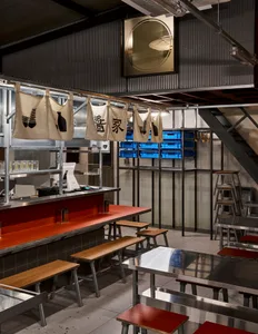 Modern Asian restaurant interior with a red bar, wooden walls, and metal accents, featuring comfortable seating and a stylish atmosphere