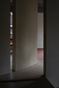 Narrow hallway with a red brick floor and white walls, featuring two archways and a dark atmosphere