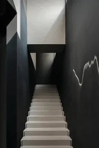 A darkened space with a concrete staircase and black railing, featuring several steps leading upwards