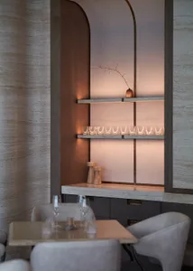 Dining area with a table and chairs, surrounded by wine glasses, in a room with marble walls and an elegant atmosphere
