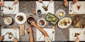 A warm and inviting dining scene with a wooden table, chairs, and various plates of food, wine glasses, and utensils