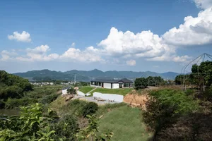 A serene outdoor seating area with a modern house in the background, surrounded by a valley and natural landscape