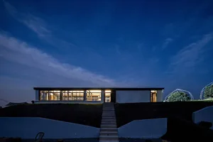A modern building with a glass facade, concrete walls, and a staircase leading to the entrance, set against a contrasting background