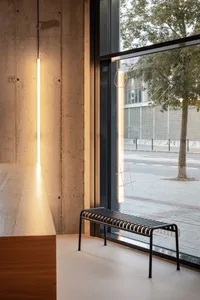 A modern restaurant interior with a metal bench in front of a window, surrounded by concrete walls and two chairs, creating a comfortable and inviting atmosphere