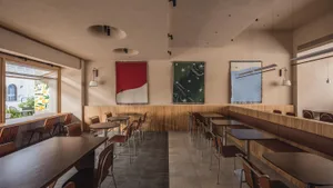 Empty restaurant interior with wooden floors and tables, well-lit with natural light and overhead lighting, featuring a mix of wood and concrete elements