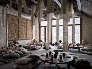 A warm and inviting dining space with a wooden ceiling, stone walls, and a round table surrounded by chairs, with vases placed throughout the space