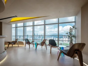 Open modern living area with a large window offering a city view, featuring unique chairs, including one resembling a boat, amidst a comfortable and inviting atmosphere