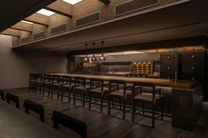 Dimly lit restaurant kitchen with a wooden bar counter and chairs, creating a cozy ambiance