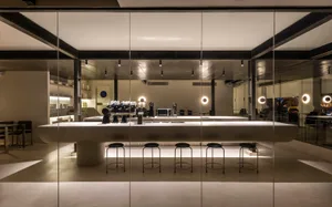 Industrial kitchen with a long countertop featuring stools, cups, and a laptop, in a clean and organized restaurant setting