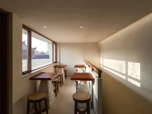 Empty restaurant with white interior, three wooden tables, and four chairs, creating a clean and inviting atmosphere