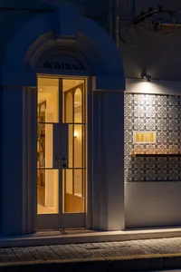 A concrete building entrance with a decorative doorway featuring glass panels and illuminated by lights