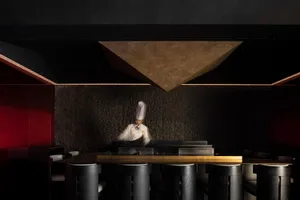 A busy restaurant kitchen with a chef preparing food on a grill, surrounded by chairs and a dining table