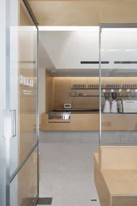 A modern coffee shop interior with a wooden counter, two chairs, and various items such as cups, bottles, and a microwave