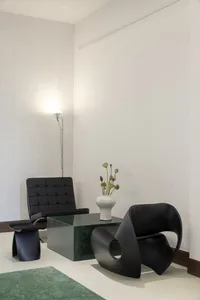 A modern living space with a leather chair in front of a glass table, surrounded by vases and a potted plant, with a clean and minimalistic atmosphere