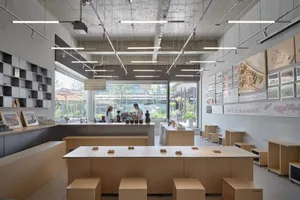 Casual restaurant interior with wooden tables and benches, multiple people sitting and standing, and a focus on socializing and enjoying food together