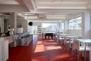 A modern restaurant interior with red tile flooring, clean lines, and natural light, featuring multiple tables and chairs in a welcoming atmosphere