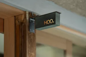 A minimalist entryway with a wooden door featuring a black sign reading Hoo, creating a warm and inviting atmosphere