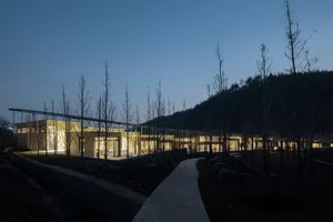 A modern building surrounded by trees at night, with glass walls allowing natural light to enter the space