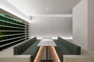 A modern restaurant interior with a wooden dining table surrounded by green-upholstered chairs, well-lit by natural and artificial light