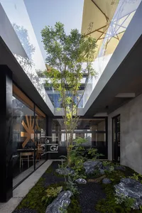 A calm and inviting indoor space with a large tree in the center, surrounded by chairs and two dining tables, with a touch of nature added to the interior design