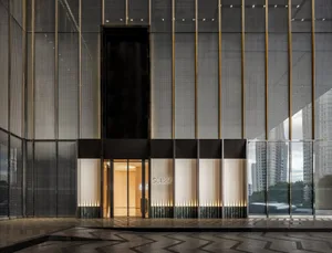 A modern building with a large glass wall, concrete structure, and two doors, with a person standing near the center