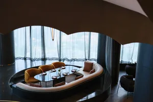 Sophisticated living space with a curved wall, seating areas, and a dining table, featuring a mix of materials and natural light