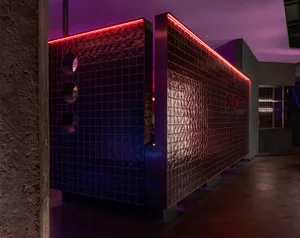 A modern interior space with a black and red glass wall, purple lighting, and two large mirrors creating a sense of depth