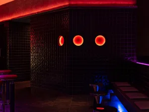 Bathroom with black walls, red accents, three round lights, a sink, and a bench, giving off a modern and sleek vibe