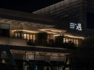 A modern glass building at night with multiple windows, surrounded by potted plants and a contemporary design