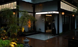 A woman walks through the entrance of an Asian-style building with a wooden structure, surrounded by potted plants and oriental design elements