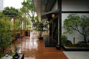 Asian-style building with wooden floors, a patio area, and natural light from a large window, surrounded by potted plants and multiple chairs