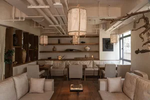 A modern living area with a dining table, multiple couches, a record player, and a bookshelf, featuring neutral tones and clean lines