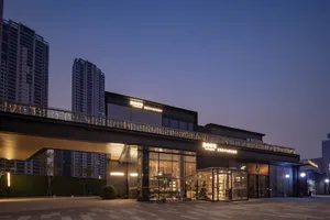 A modern glass building at night with a sophisticated ambiance, featuring a steel and glass facade, potted plants, and outdoor seating area