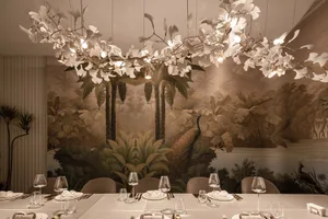 Dining area with a long table, chairs, wine glasses, and utensils, surrounded by palm trees in the background