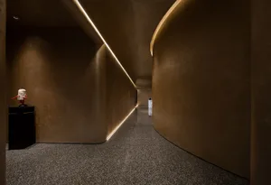 A long, curved hallway with a brown color scheme, lit by lights on both sides and featuring a person standing in the center