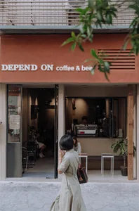 A cozy coffee shop interior with red brick walls, potted plants, and seating areas with chairs and dining tables, featuring a mix of people and a warm atmosphere