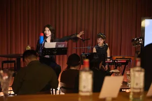 A woman sings into a microphone on stage in front of a lively audience at a bar