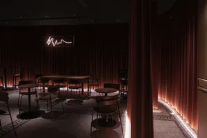 Dimly lit dining space with tables and chairs in various positions, featuring brown and orange-toned walls and a warm ambiance