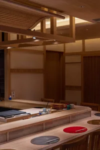 Warm and inviting Asian restaurant interior with wooden floors and walls, featuring chairs and tables with cups and a bowl